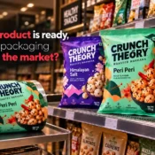 Packaging Material Supplier showing colourful printed snack pouches for roasted makhana in different flavours alongside a matching flexible packaging film roll on a supermarket shelf