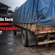 Worker securing a heavy-duty blue tarpaulin over a loaded transport truck using ropes and metal eyelets, highlighting the Best Tarpaulin Brand in India for cargo protection.